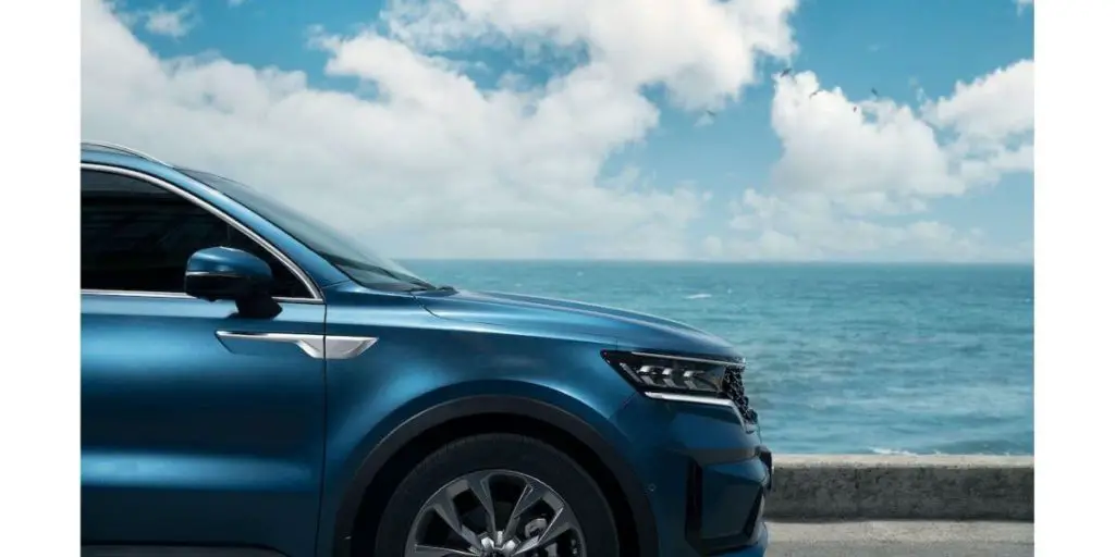 The image presents a captivating coastal landscape featuring a luxurious blue Kia Sorento SUV