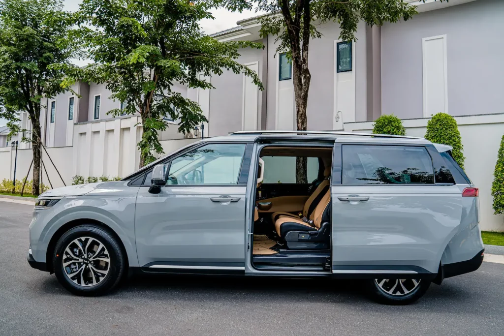 side view of grey 2023 Kia Carnival parked in front of the building with the sliding doors open