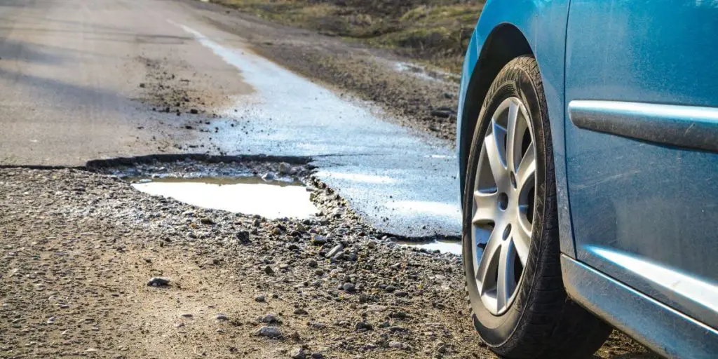 blue car driving on the bumpy road with potholes